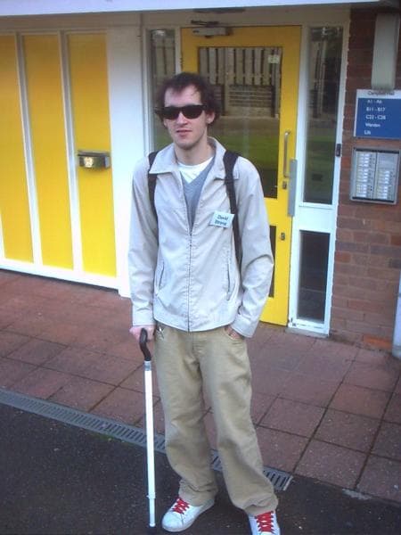 James standing with his white cane and sunglasses